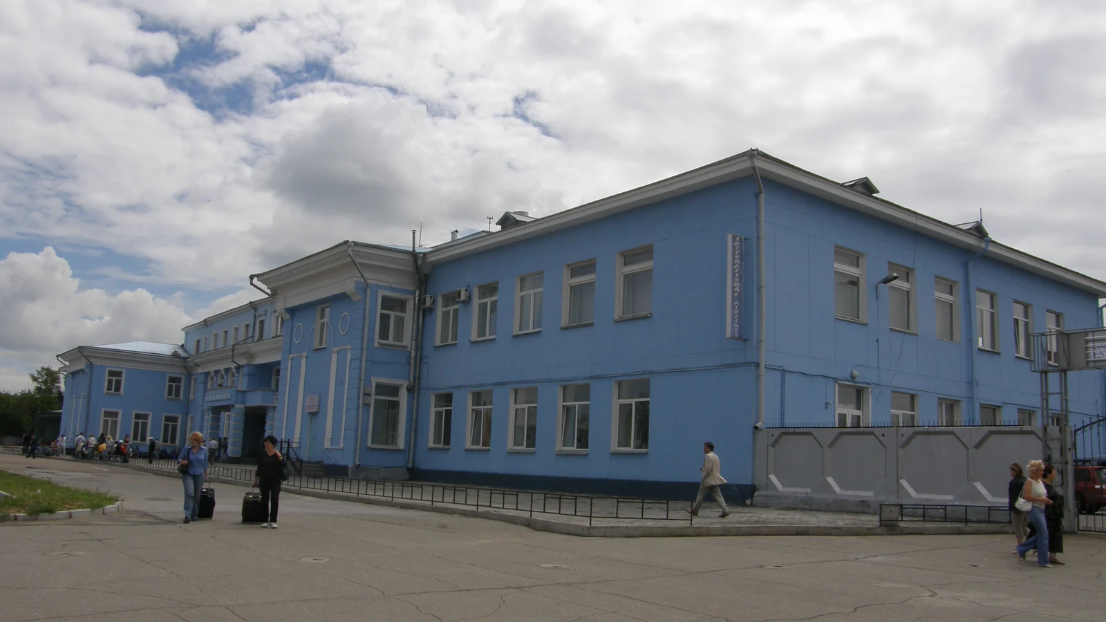 Голубое здание международного терминала аэропорта Иркутска, рядом идут пассажиры